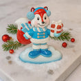 Load image into Gallery viewer, Christmas-themed figurine of a fox in winter clothing with a gift, surrounded by festive decorations on a white background.
