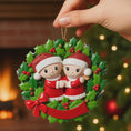 Load image into Gallery viewer, Christmas ornament with couple in a wreath held by a hand against a festive background.
