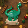 Load image into Gallery viewer, Green dinosaur ornament on a wooden surface with Christmas decorations
