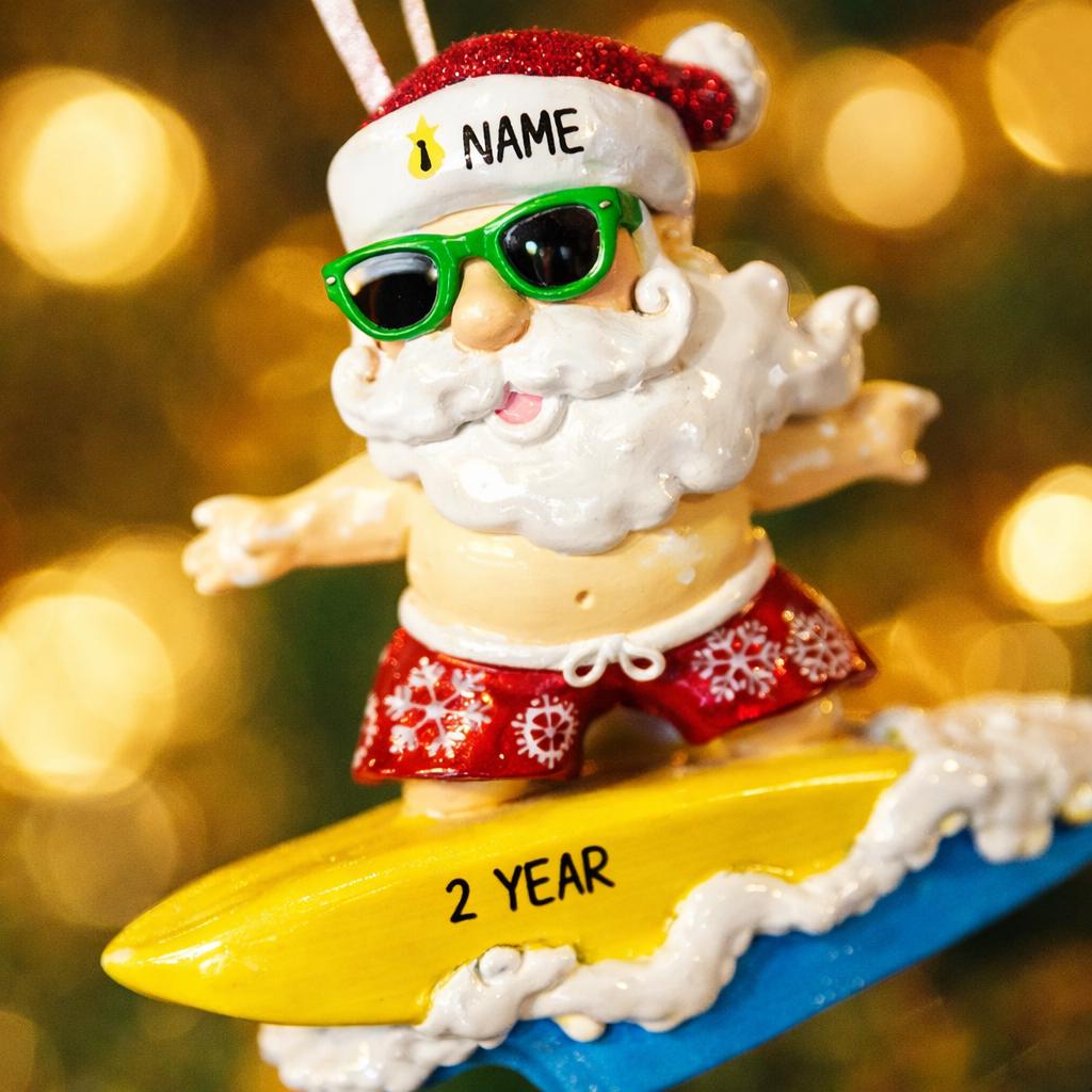 Personalized surfing Santa Christmas ornament featuring a fun beach themed Santa riding a wave on a surfboard. Raised 3D front details add depth while the back remains flat for easy hanging. Custom name and year placement make this ornament a playful and unique holiday keepsake for Christmas tree decor.