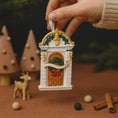 Load image into Gallery viewer, Decorative Christmas ornament resembling a door with wreath and bow, held by a hand against a festive background.
