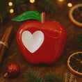 Load image into Gallery viewer, Red apple-shaped container with a white heart on a wooden surface with Christmas decorations.
