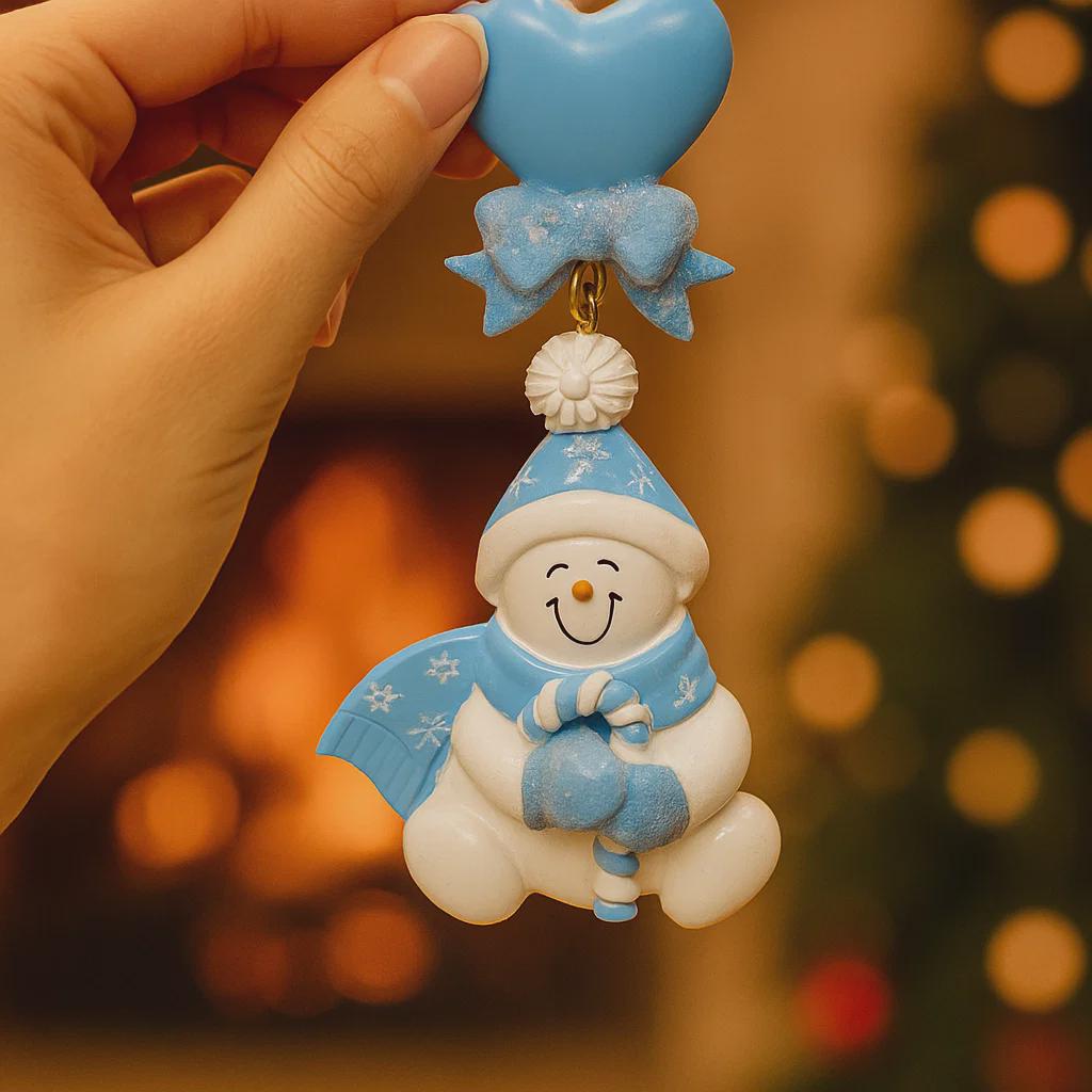 Snowman keychain with blue hat and scarf held by a hand against a blurred festive background.