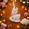 Load image into Gallery viewer, A glossy resin baby girl llama ornament features a white smiling llama with soft pink accents, raised textured fur details, pink bow and scarf elements, glitter highlights, and a smooth painted cartoon style finish, styled with warm holiday lights and nursery themed props, handwritten personalization showing the baby name on the front banner and the year placed on the llama body, designed as a mostly 2D ornament with raised 3D details on the front only.
