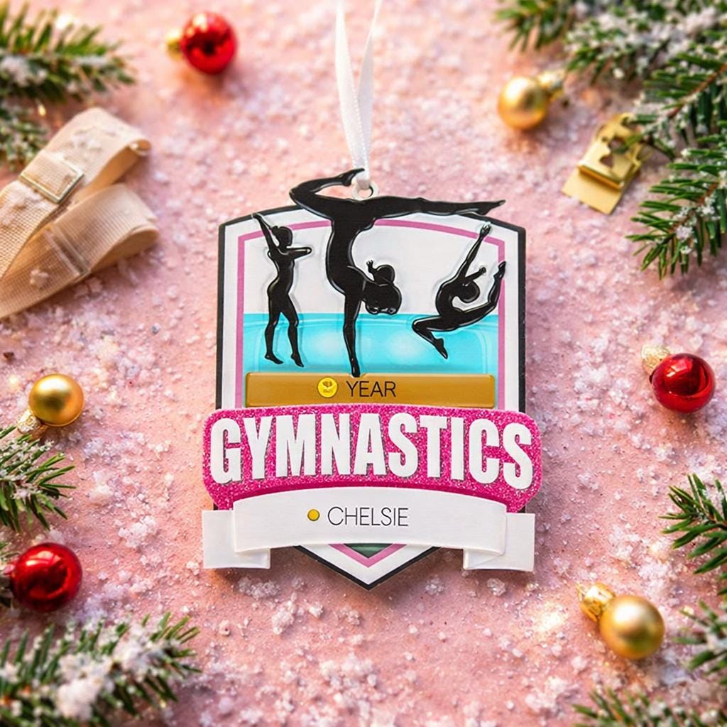 Personalized gymnastics Christmas ornament featuring elegant gymnast silhouette figures in motion, customizable name area on the front banner and customizable year area above the banner, glossy finish with raised 3D front details and flat 2D back, white hanging ribbon, displayed on a soft pink snowy holiday background with festive ornaments greenery and warm Christmas decor.
