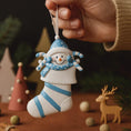 Load image into Gallery viewer, Hand holding a decorative snowman ornament with a blue hat and scarf against a festive background.
