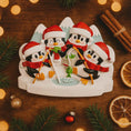 Load image into Gallery viewer, Decorative Christmas ornament with penguins on a wooden surface with festive decorations.
