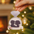 Load image into Gallery viewer, Decorative ornament with silhouettes of a couple and flowers, held by a hand against a festive background.
