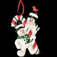 Load image into Gallery viewer, Christmas ornament featuring two snowmen holding a candy cane with a cardinal on top against a black background.
