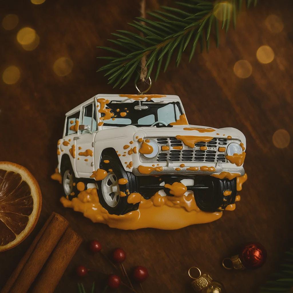 Decorative ornament shaped like a white SUV with orange mud splashes on a wooden surface with festive decorations.