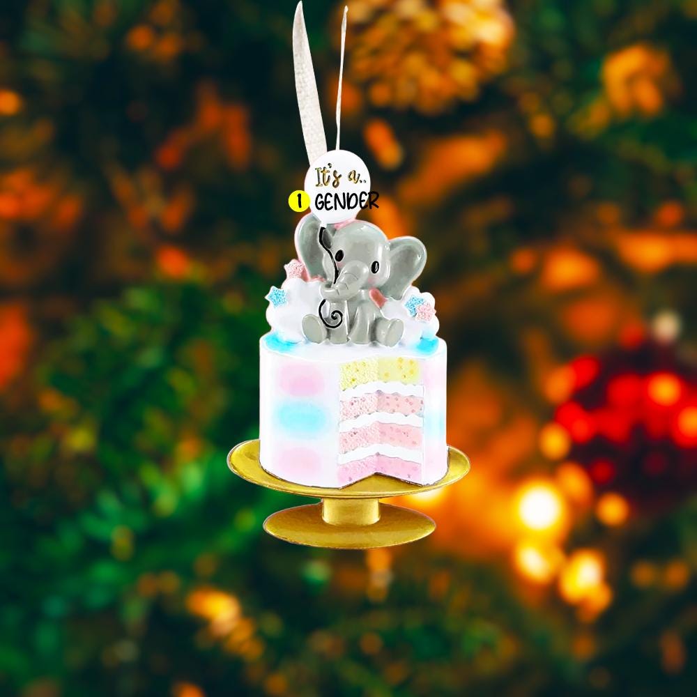 Personalized gender reveal Christmas ornament for baby girl featuring a pastel cake design with a cute elephant topper and its a gender message, soft pink and blue tones with layered cake details and glossy finish, styled as a sweet holiday keepsake for expecting parents, baby announcement and first Christmas memories, displayed on a warm wooden background with cozy Christmas lights, baby shoes and festive decor creating a joyful and heartwarming celebration scene
