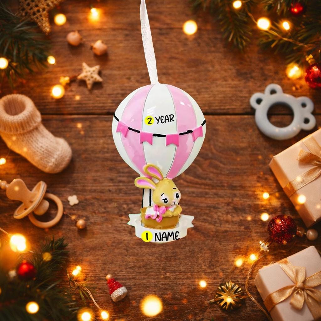 A personalized baby girl ornament featuring a cute bunny riding a pastel pink hot air balloon. Soft pink and white tones with delicate bow details create a sweet and cozy look. Handwritten personalization includes baby name and year. Mostly 2D ornament with raised 3D details on the front only, lightweight and easy to hang, perfect for baby first Christmas, nursery decor, and toddler keepsakes.