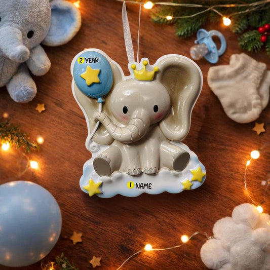 Decorative elephant ornament with a blue balloon and crown, surrounded by festive decorations on a wooden surface.