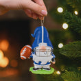 Load image into Gallery viewer, Personalized football gnome Christmas ornament featuring a blue and white gnome character wearing a football helmet and holding a football, customizable name area on the front body and customizable year area on the football, glossy finish with raised 3D front details and flat 2D back, white hanging ribbon, displayed on a snowy football field themed holiday background with pine branches and festive decorations.
