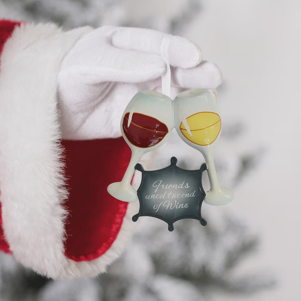 Decorative ornament with wine glasses and a bottle labeled 'Friends unite around wine' held by a gloved hand.