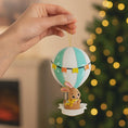 Load image into Gallery viewer, A personalized baby boy ornament featuring a cute bunny riding a pastel blue hot air balloon. Soft blue and white tones with gentle decorative details create a calm and cozy look. Handwritten personalization includes baby name and year. Mostly 2D ornament with raised 3D details on the front only, lightweight and easy to hang, perfect for baby first Christmas, nursery decor, and toddler keepsakes.
