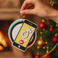 Load image into Gallery viewer, Decorative ornament shaped like a smartphone with a tiktok logo on a Christmas tree and fireplace background.
