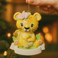 Load image into Gallery viewer, Personalized baby lion Christmas ornament featuring a sweet yellow lion cub wearing a floral crown and holding a small leaf. The bottom banner can be customized with name and year, creating a unique keepsake for a newborn or toddler. Designed in warm yellow and soft pastel tones, this resin baby Christmas ornament is perfect for celebrating Baby’s First Christmas or adding a personalized jungle themed touch to your holiday tree.
