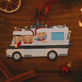Load image into Gallery viewer, Christmas ornament of a family in a car with children wearing Santa hats on a wooden surface.
