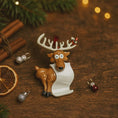 Load image into Gallery viewer, Decorative reindeer ornament with a piece of paper on a wooden surface with Christmas decorations.
