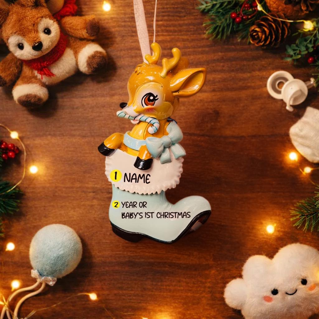 A glossy resin baby deer ornament features a cute fawn character sitting inside a soft pastel blue winter boot, holding a striped candy cane, with gentle antler details, smooth painted cartoon style finish, soft holiday lighting and blurred festive background, handwritten personalization showing the baby name on the boot and the year or Baby’s First Christmas text below, designed as a mostly 2D ornament with raised 3D details on the front only.