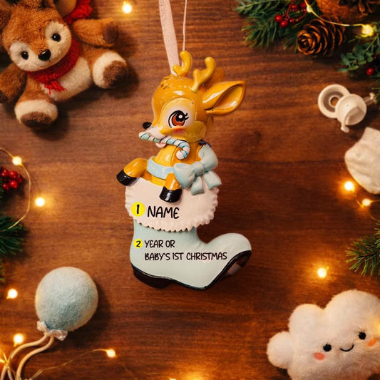 A glossy resin baby deer ornament features a cute fawn character sitting inside a soft pastel blue winter boot, holding a striped candy cane, with gentle antler details, smooth painted cartoon style finish, soft holiday lighting and blurred festive background, handwritten personalization showing the baby name on the boot and the year or Baby’s First Christmas text below, designed as a mostly 2D ornament with raised 3D details on the front only.