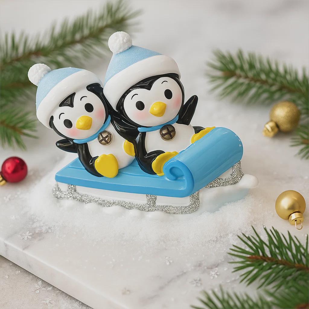 Two penguin figurines on a blue sled with Christmas decorations in the background.