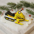 Load image into Gallery viewer, Yellow snowmobile ornament on a decorative base with Christmas decorations
