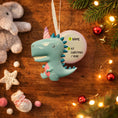 Load image into Gallery viewer, Decorative ornament with a unicorn dinosaur design on a wooden surface with Christmas decorations.
