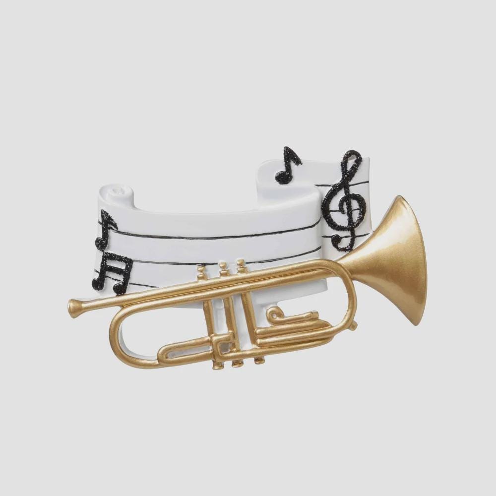 Personalized music ornament featuring a white musical staff design with black notes and a gold trumpet detail. Includes free handwritten personalization with one name and year written on the sheet music. Shown hanging with a ribbon in a warm festive holiday setting with soft lights instruments and seasonal decor. Designed with a 3D raised front and flat back perfect for Christmas tree display and gifts for musicians music lovers and band members.