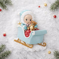 Load image into Gallery viewer, Personalized baby first Christmas ornament featuring a sweet baby boy sitting in a pastel blue sleigh holding a small teddy bear. Handwritten baby name and year displayed on the sleigh front. Smooth resin finish with soft winter tones, lightweight structure, mostly 2D ornament with raised 3D front details, designed for baby boy nursery themed Christmas tree decor and keepsake gifting.
