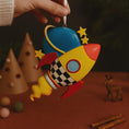 Load image into Gallery viewer, Colorful rocket-shaped ornament held by a hand with a dark background
