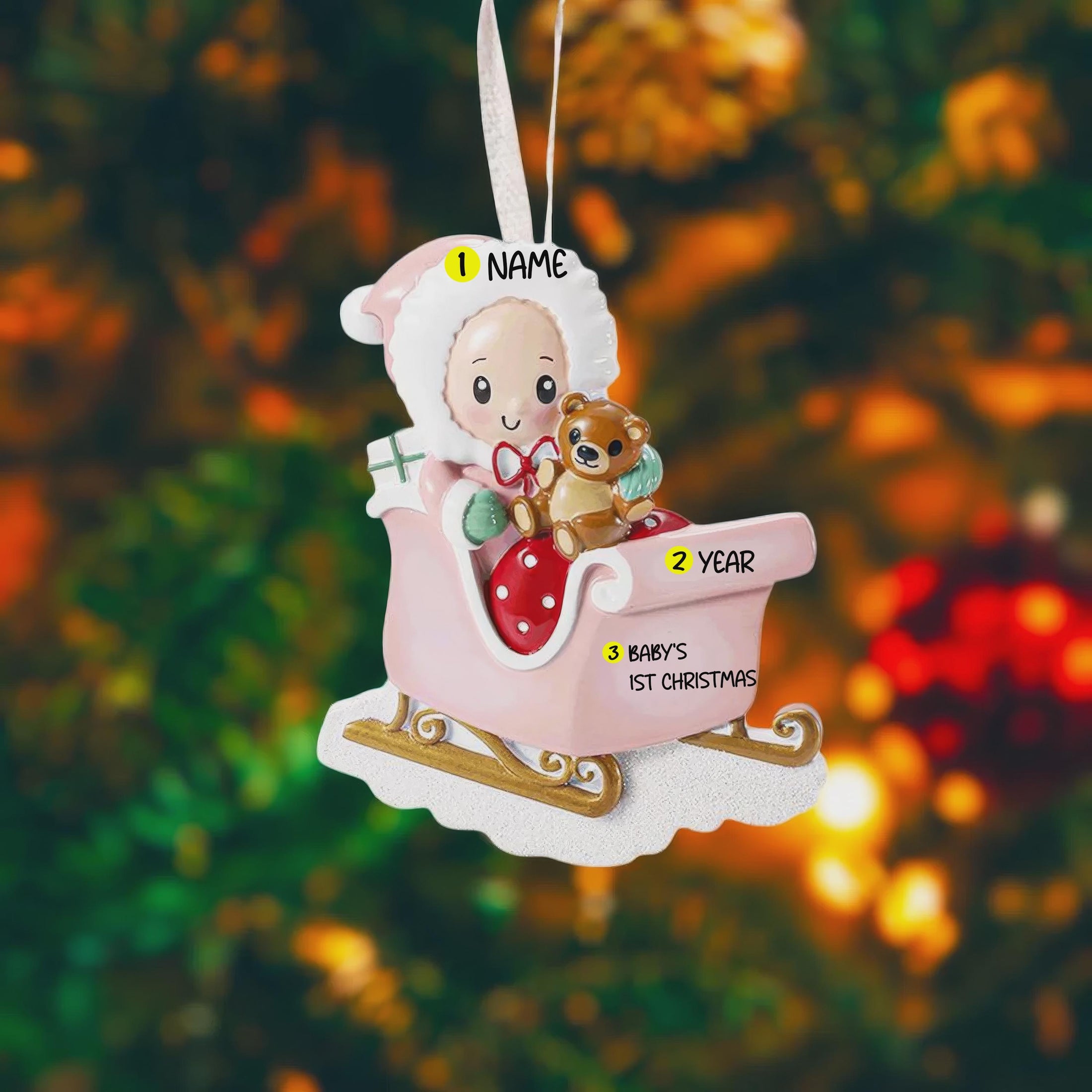 Personalized baby first Christmas ornament featuring a sweet baby sitting in a pastel pink sleigh holding a teddy bear. Handwritten baby name and year or Baby’s First Christmas text shown on the sleigh. Smooth resin finish with soft pastel tones, lightweight structure, mostly 2D ornament with raised 3D front details, designed for baby nursery themed Christmas tree decor and keepsake gifting.