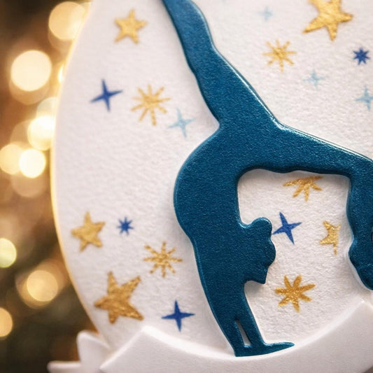 Personalized gymnastics Christmas ornament featuring an oval white design with a navy blue gymnast silhouette performing a handstand pose, surrounded by gold and blue star accents, customizable year displayed on the upper area, customizable name space on the bottom banner, smooth glossy finish with raised 3D front details and flat 2D back, white hanging ribbon, photographed on a soft pink snowy holiday background with winter greenery, festive ornaments, and warm seasonal styling.
