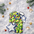 Load image into Gallery viewer, A glossy resin Army soldier uniform ornament in green brown and blue camouflage colors features a military jacket and pants shape with raised buttons and pockets, white and blue star accents, light snow texture, a smooth painted cartoon style finish, and handwritten personalization showing a name and year on the attached tag, designed as a mostly 2D ornament with raised 3D details on the front only for Christmas tree decor.

