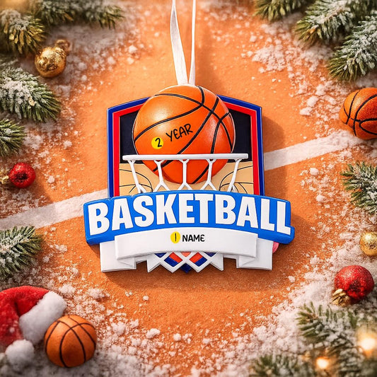 Personalized basketball Christmas ornament featuring an orange basketball and hoop design with customizable name area on the front banner and customizable year area on the basketball, glossy finish with raised 3D front details and flat 2D back, white hanging ribbon, displayed on a snowy basketball court themed holiday background with pine branches and festive decorations.