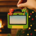 Load image into Gallery viewer, Decorative ornament with a dinosaur and tropical elements on a green background, held by a hand.
