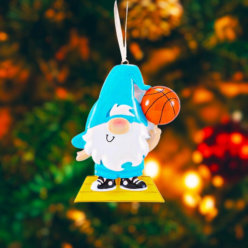 Personalized basketball gnome Christmas ornament featuring a cute blue gnome character holding a basketball, customizable name area on the hat and customizable year area on the base, glossy finish with raised 3D front details and flat 2D back, white hanging ribbon, displayed on a snowy holiday background with pine branches and festive decorations.
