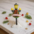 Load image into Gallery viewer, Decorative Christmas street lamp with lights on a snowy surface with ornaments and greenery.
