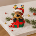 Load image into Gallery viewer, Decorative reindeer figurine with a gift on a snowy surface with Christmas decorations.
