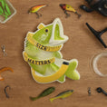Load image into Gallery viewer, Fishing-themed decorative ornamentwith a fish and 'Size Matters' text on a wooden surface with fishing equipment.
