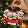 Load image into Gallery viewer, Decorative Christmas ornament of four polar bears in a red car with lights, held against a blurred Christmas tree background.
