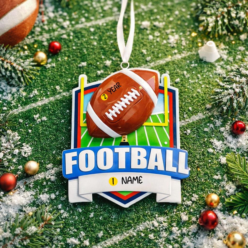 Personalized football Christmas ornament featuring a brown football with stitched details on a shield style background and goalpost design, customizable name area on the front banner and customizable year area on the football, glossy finish with raised 3D front details and flat 2D back, white hanging ribbon, displayed on a snowy football field themed holiday background with pine branches and festive decorations.