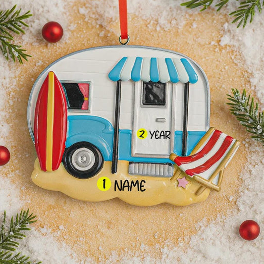 Decorative ornament shaped like a camper with a surfboard and beach chair on a sandy background.