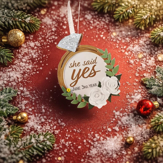 Elegant engagement Christmas ornament featuring gold accents white florals and the phrase she said yes. Personalized with a custom date to commemorate a proposal or engagement moment. A romantic keepsake perfect for celebrating newly engaged couples weddings and meaningful holiday memories.