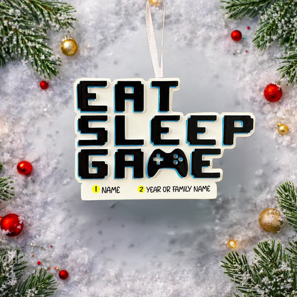 Personalized Eat Sleep Game Christmas ornament with a raised 3D front featuring bold block-style lettering and a detailed game controller icon. The front design is fully three dimensional, creating depth and texture, while the back is flat 2D for easy hanging and durability. White base with black raised letters and subtle colored accents. Includes hand-added personalization with name and year or family name. Gaming-themed holiday ornament displayed on snowy festive background with warm lights, designed for 