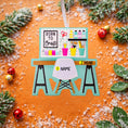 Load image into Gallery viewer, ornament featuring a creative desk scene with colorful craft supplies including scissors paint bottles brushes pencils and storage cups. The ornament showcases a playful crafting workspace design with a modern chair and desk setup. Made from durable resin with a detailed 3D front and flat 2D back for smooth hanging. Includes free handwritten
