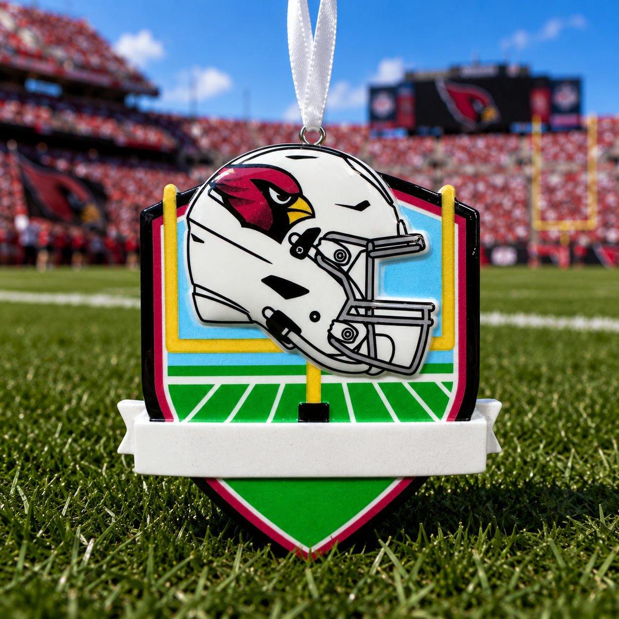 Arizona Cardinals football helmet ornament displayed on a green football field with stadium stands in the background.