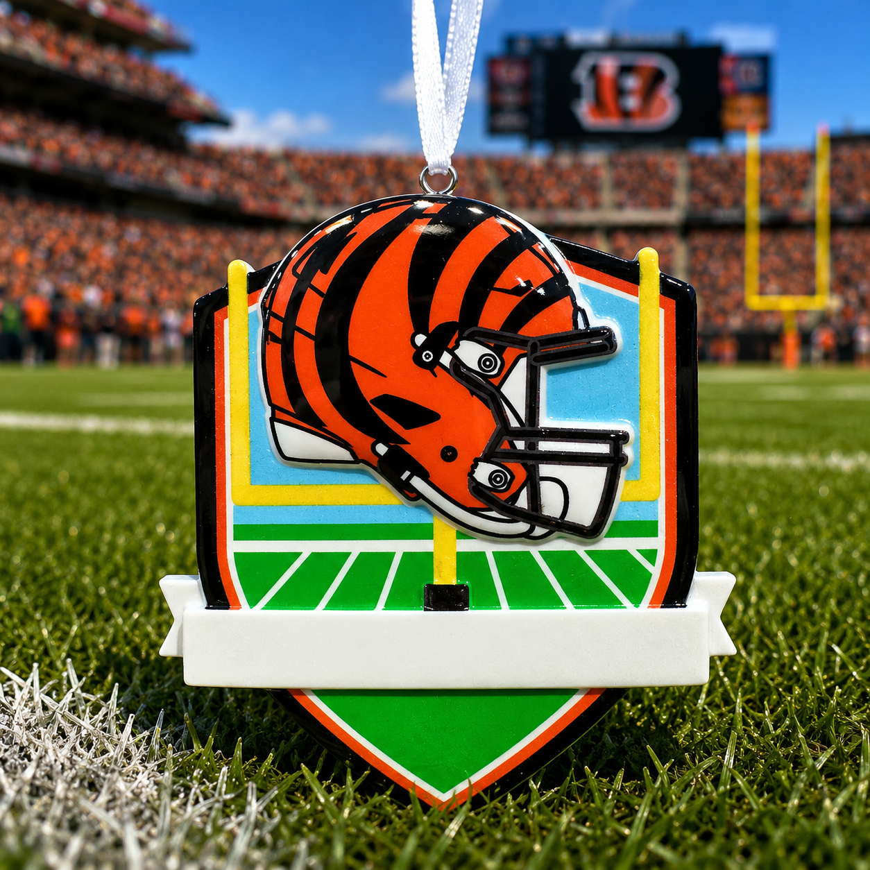 A Cincinnati Bengals themed ornament shaped like a football helmet over a football field, displayed on grass with a blurred stadium background.